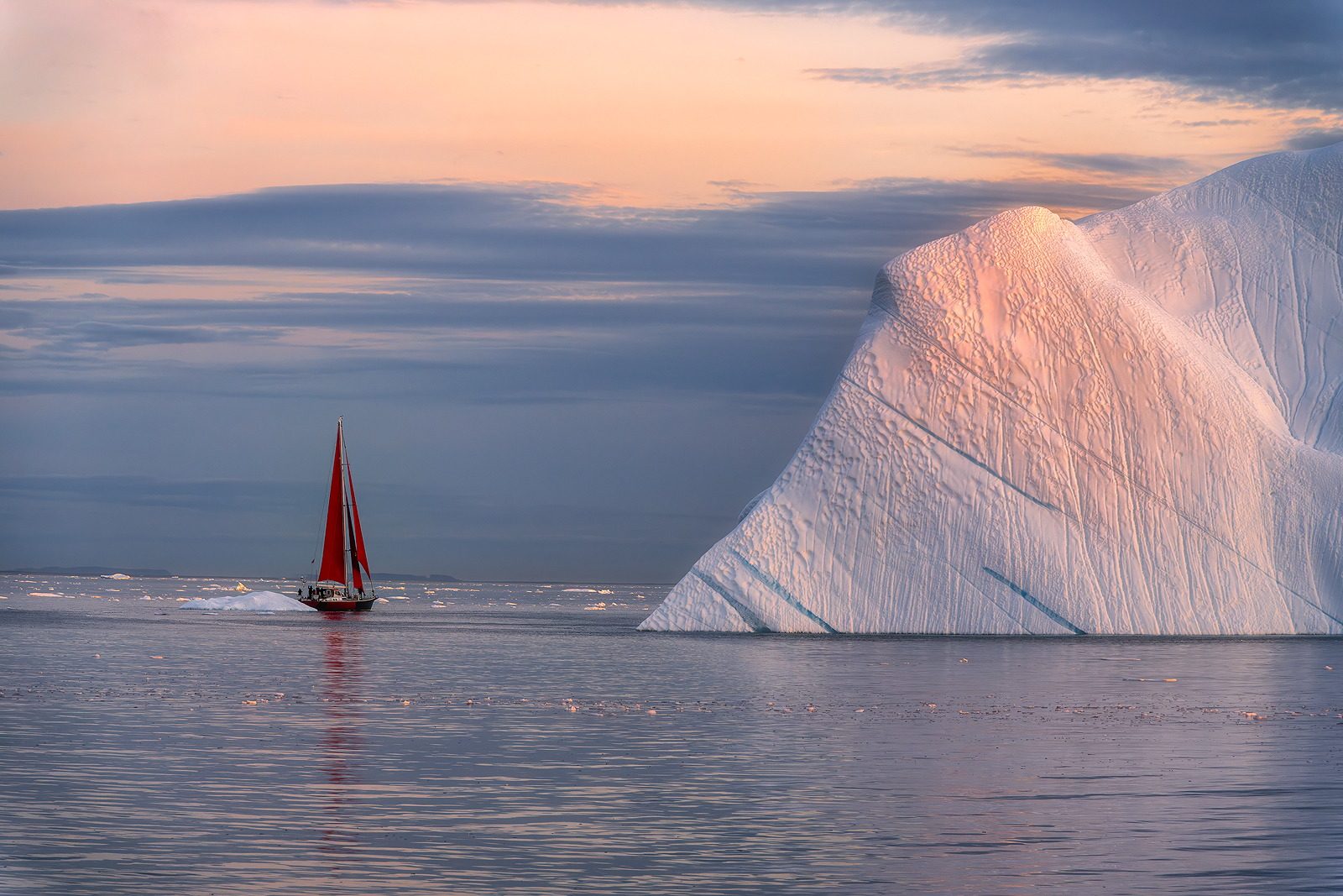 Red sails beside a pyramid iceberg